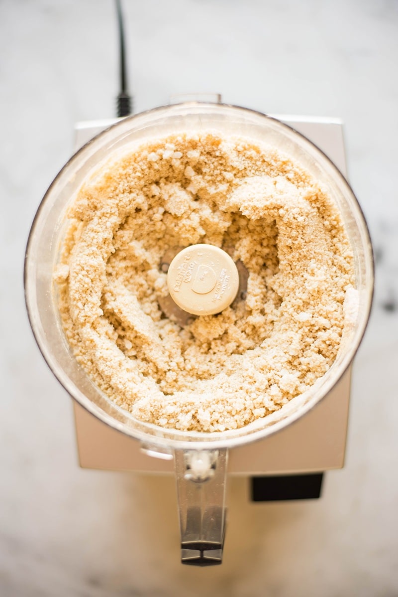 Overhead image of a food processor, filled with ingredients mixed to make a flaky pie crust.