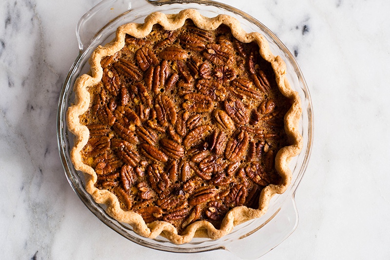 Overhead image of a glass pie dish containing a Healthy Pecan Pie not yet cut into.