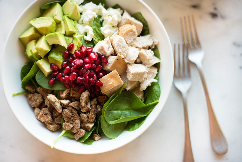 Close-up horizontal image of the leftover turkey salad. Can see the texture of the salad, including the turkey, avocado, spinach, pecans, goat cheese, and pomegranate seeds., all ready to be drizzled with the fresh cranberry vinaigrette.