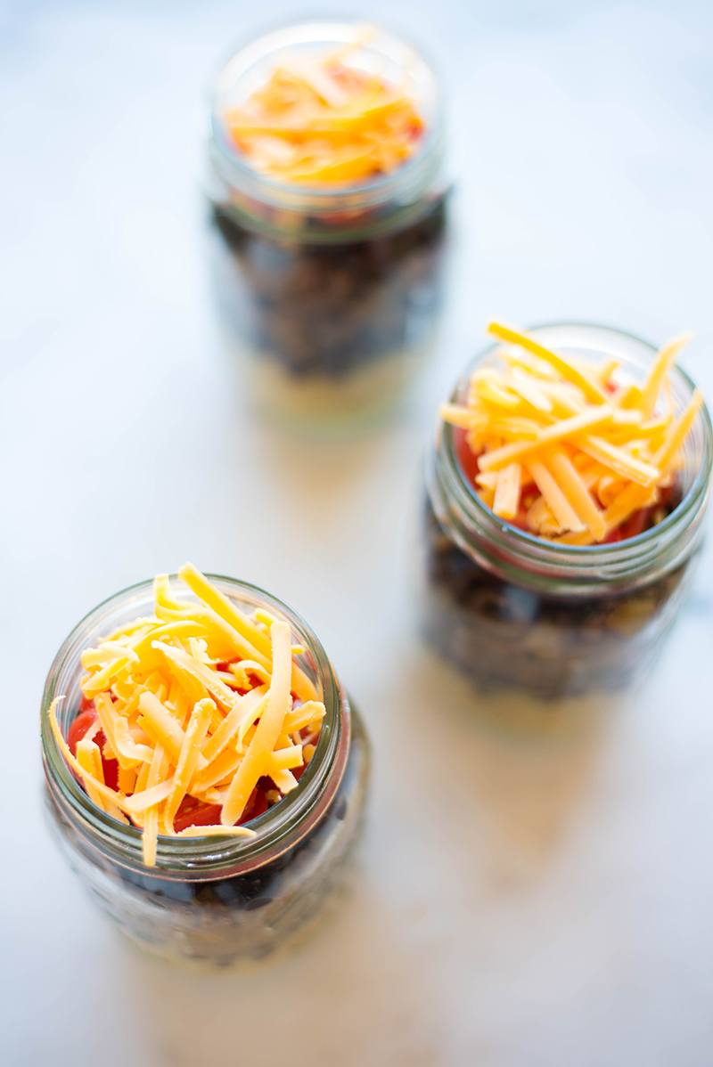 An overhead close up image of the Quinoa Taco Bowl recipe in mason jars, ready to store including quinoa, black beans and cheese.