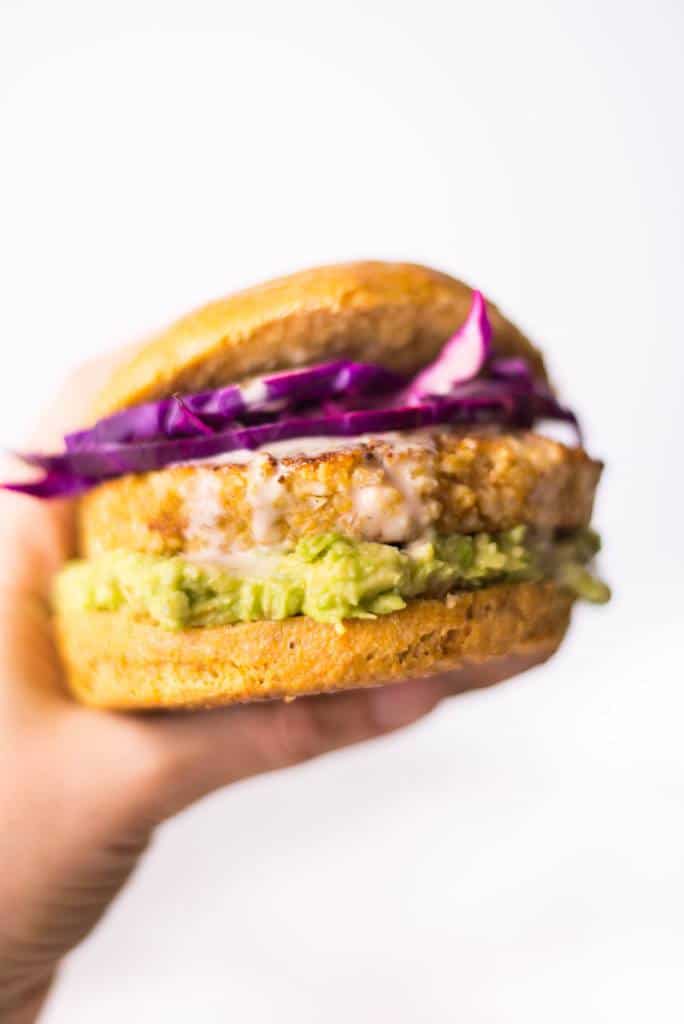 Close up image of a hand holding a spicy cauliflower burger, dressed with avocado and red onion.