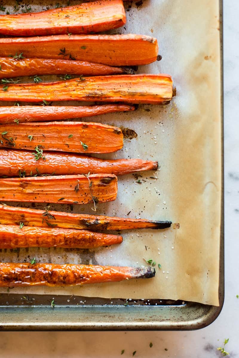 Close up of thyme-roasted carrots placed on a lined baking sheet 