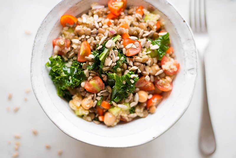 High angle photo of quinoa lentil salad with lemon vinaigrette, can see the kale, tomatoes, quinoa, garbanzo beans, and lentils, topped with sunflower seeds.