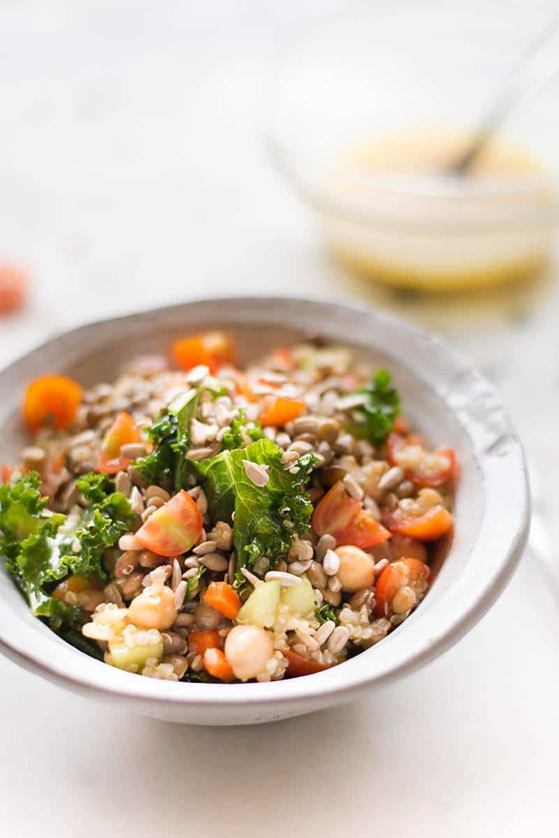 Close up image of a quinoa lentil salad in a white bowl, containing kale, lentils and tomatoes.