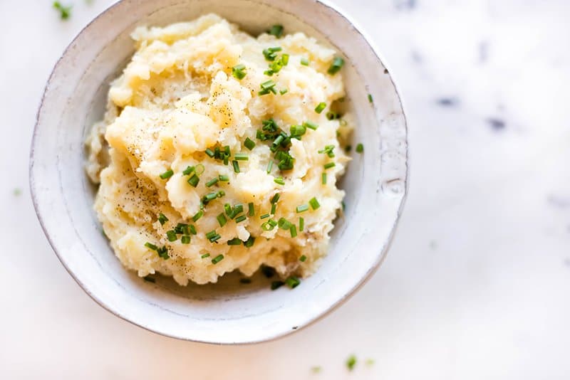 Overhead image of a white bowl filled with crock pot mashed potatoes that are garnished with chives.