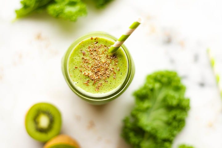 Overhead image of a kale and kiwi smoothie in a mason jar; a sliced kiwi and kale leaves are beside.