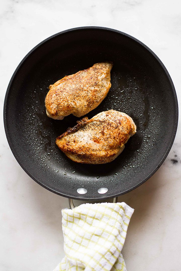 Overhead image of two chicken breasts in a skillet, cooked and ready to be used in a recipe.
