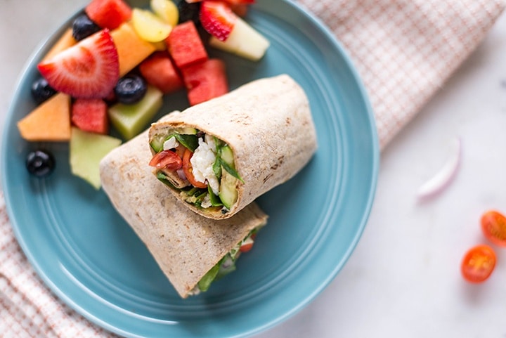 Close up image of a blue plate with a breakfast wrap and fresh fruit on the plate.
