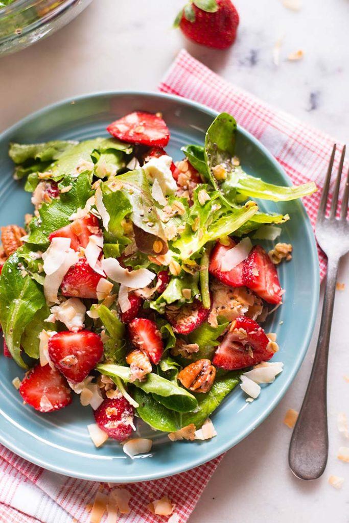 Overhead view of a strawberry and spinach salad garnished with vinaigrette and walnuts.