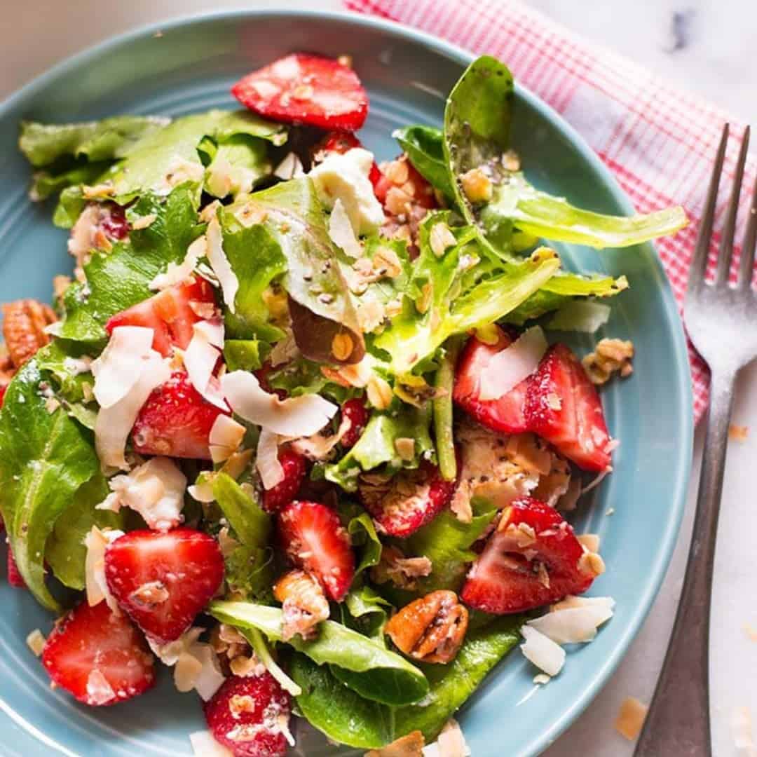 Overhead view of a blue plate with spinach and strawberry salad, garnished with walnuts.