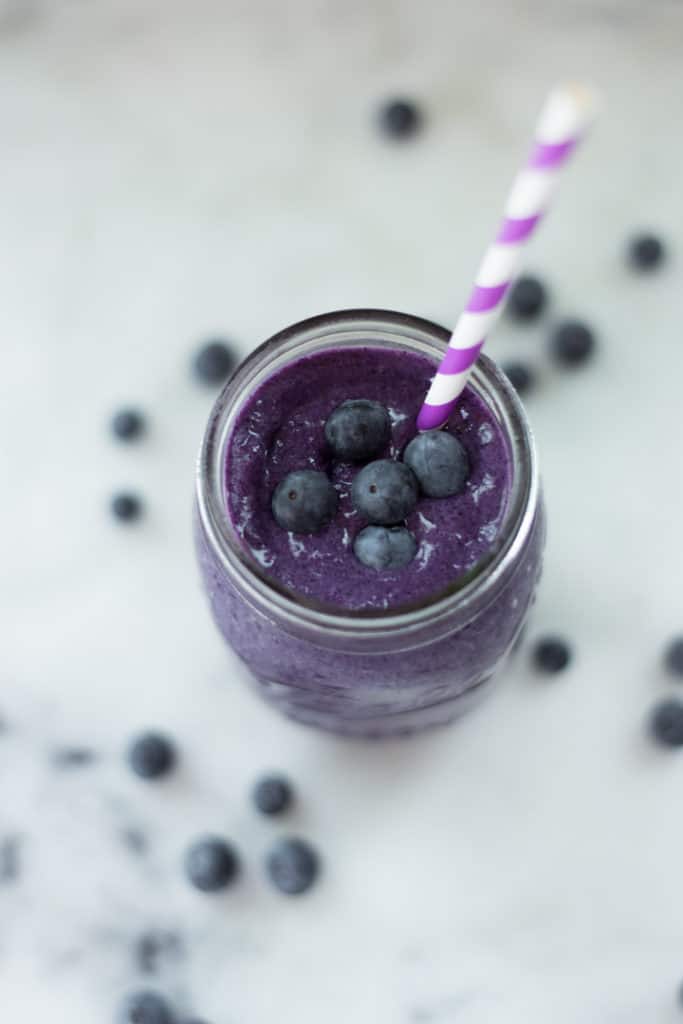Overhead view of the Fit + Slim Smoothie in a mason jar, with a striped straw in the jar and whole blueberries sprinkled in and around the jar.