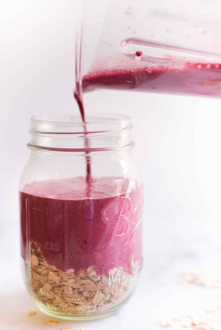 Pouring the blackberry cobbler mixture from the kitchen blender into the mason jar with the rolled oats and chia seeds.