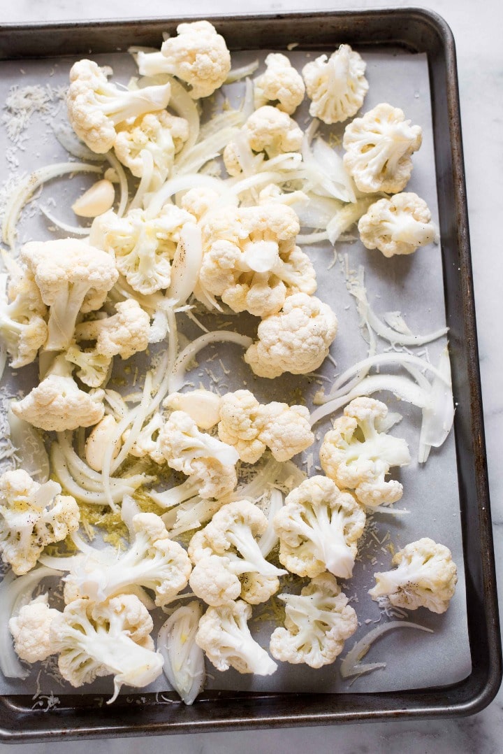 Cauliflower topped with Parmesan Cheese, Garlic, Olive Oil, and Onion on a Cookie Sheet Pan Pre-Oven