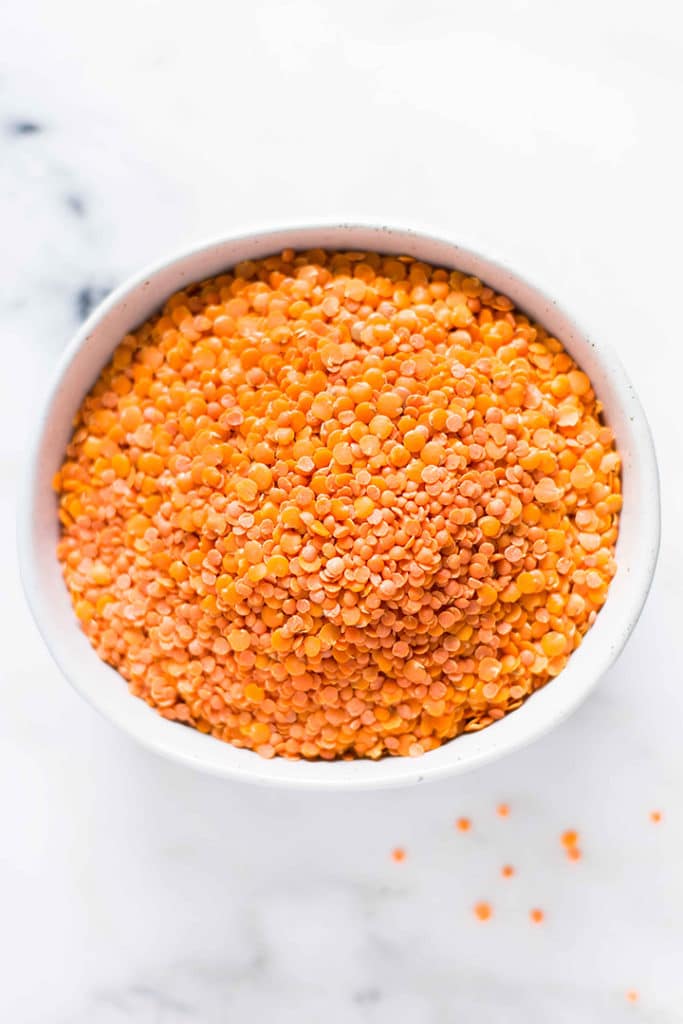 Overhead image of a bowl of dried split red lentils on a marble countertop.