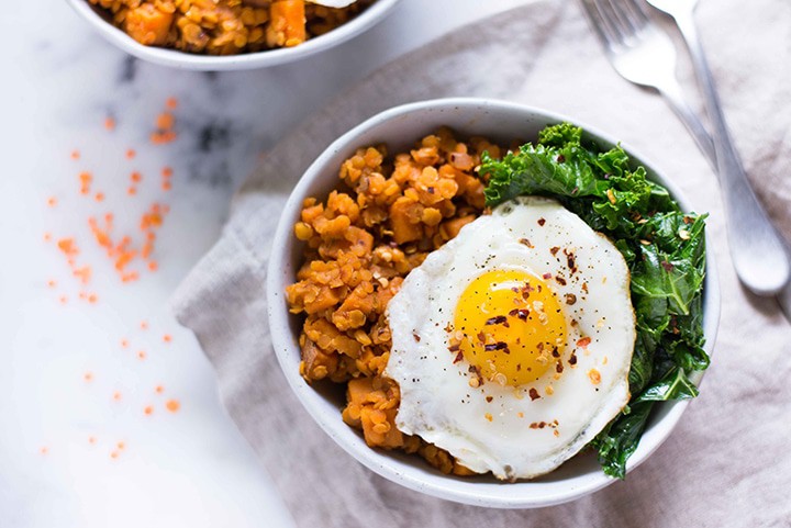 Close up of white bowl filled with sweet potato and lentil hash next to sauteed garlic kale and topped with a fried egg