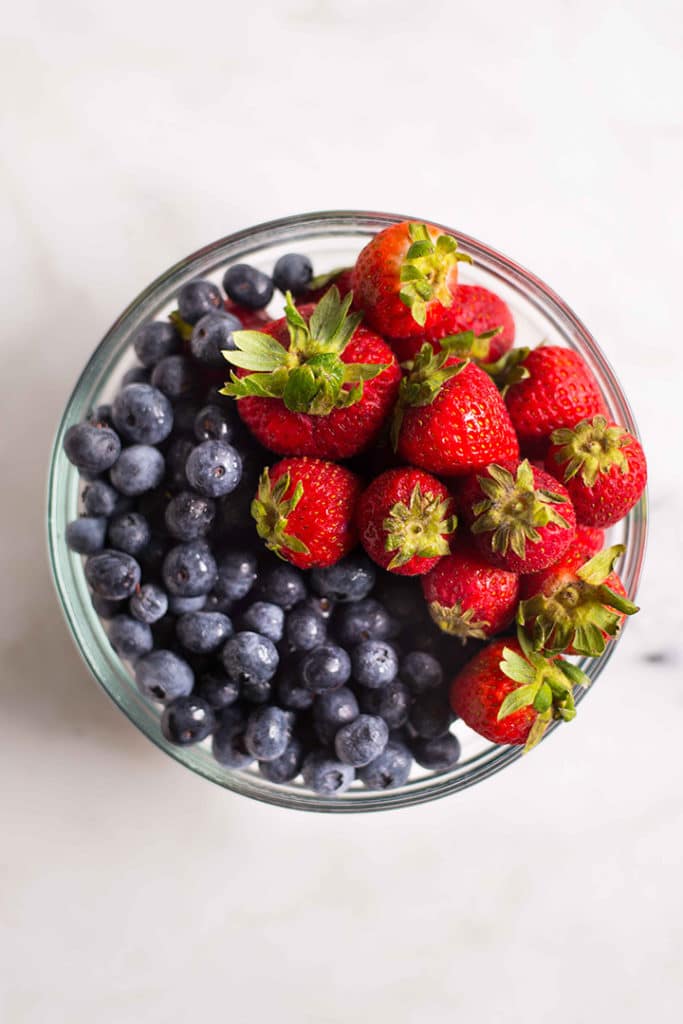 Glass bowl of fresh strawberries and blueberries, fruits that you can enjoy at home rather than processed sugar products.