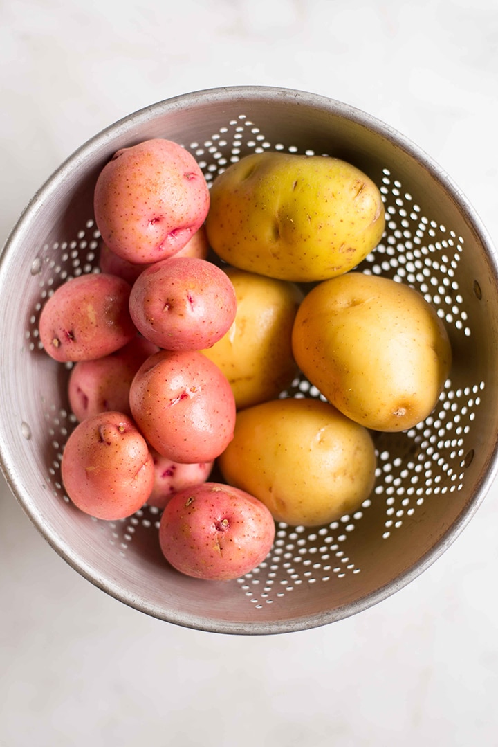 Metal colander holding raw red potatoes and yukon gold potatoes, ready to be cut into chunks for Healthy Potato Soup.