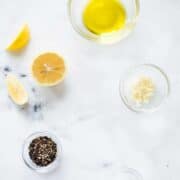 Ingredients separated for lemon pepper chicken marinade, including lemon zest, lemon juice, garlic, crushed black peppercorns, sea salt, and olive oil.