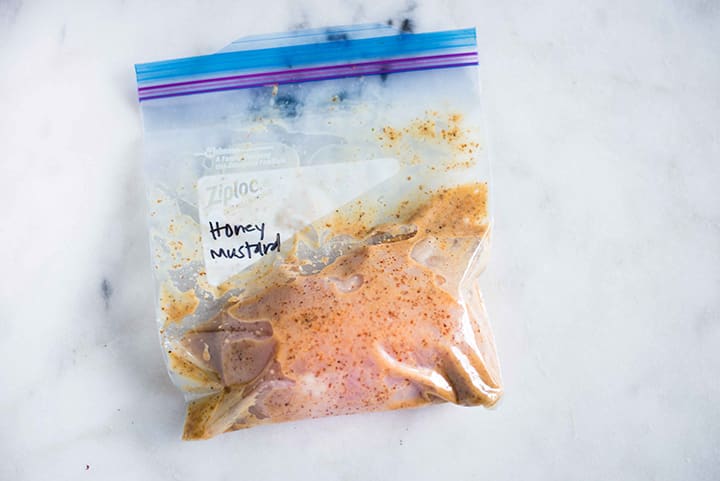 Sealable freezer bag with chicken breast and honey mustard chicken marinade, marinating and ready to cook.