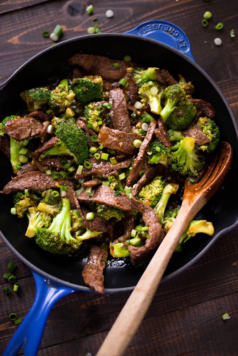 Overhead image of a blue skillet containing Healthy Beef With Broccoli ready to serve, with a wooden spoon in the skillet also.