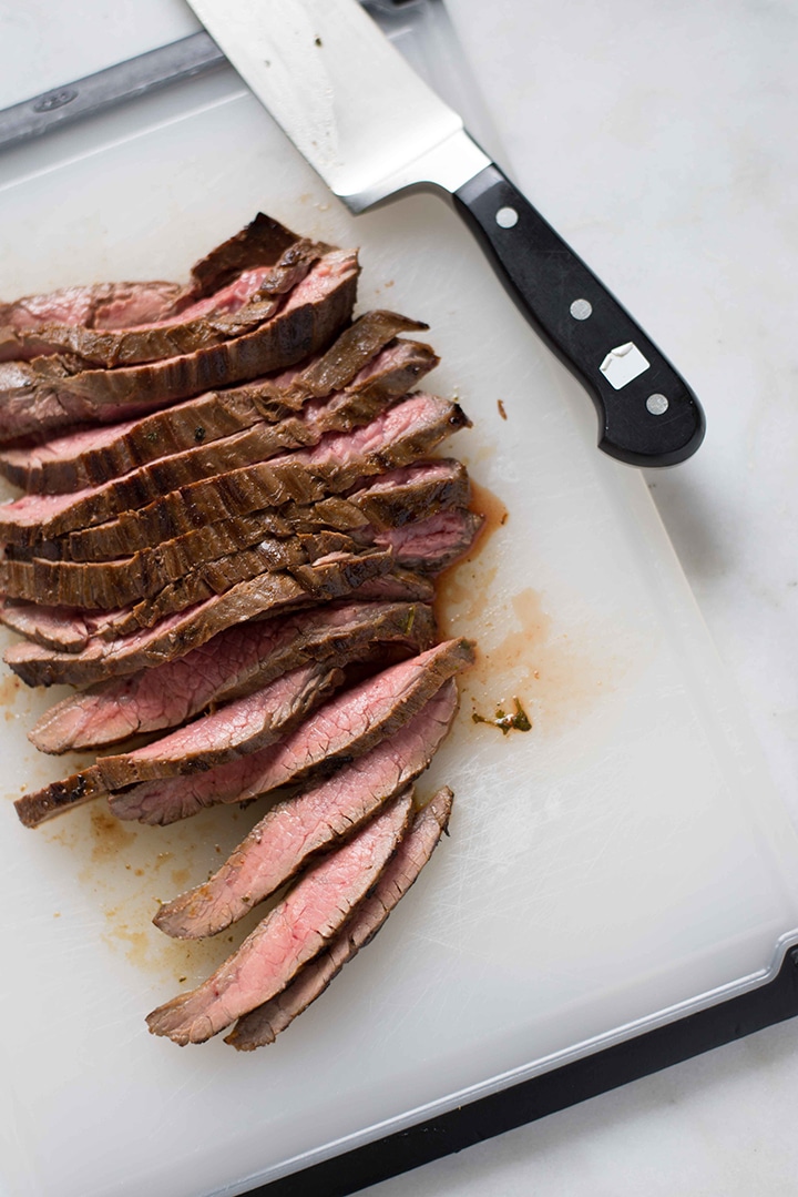 Thinly sliced marinated flank steak on a cutting board, ready to top the cilantro lime rice for the steak fajita bowl.
