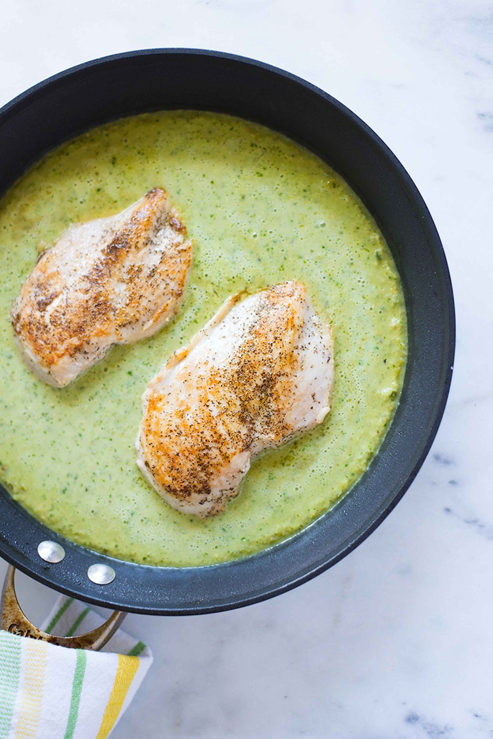 Large skillet with seasoned chicken breast and surrounded by by salsa verde, ready to cook.