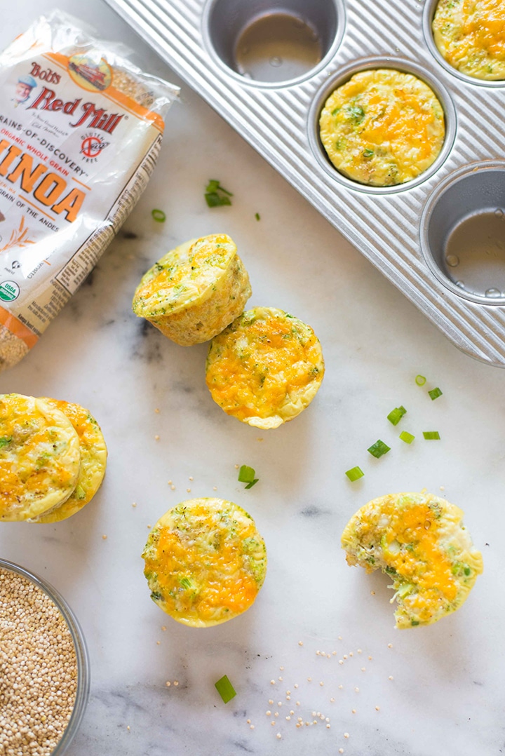 Baked healthy egg muffins laying on a counter, next to sliced green onions and quinoa, baked and ready to eat.