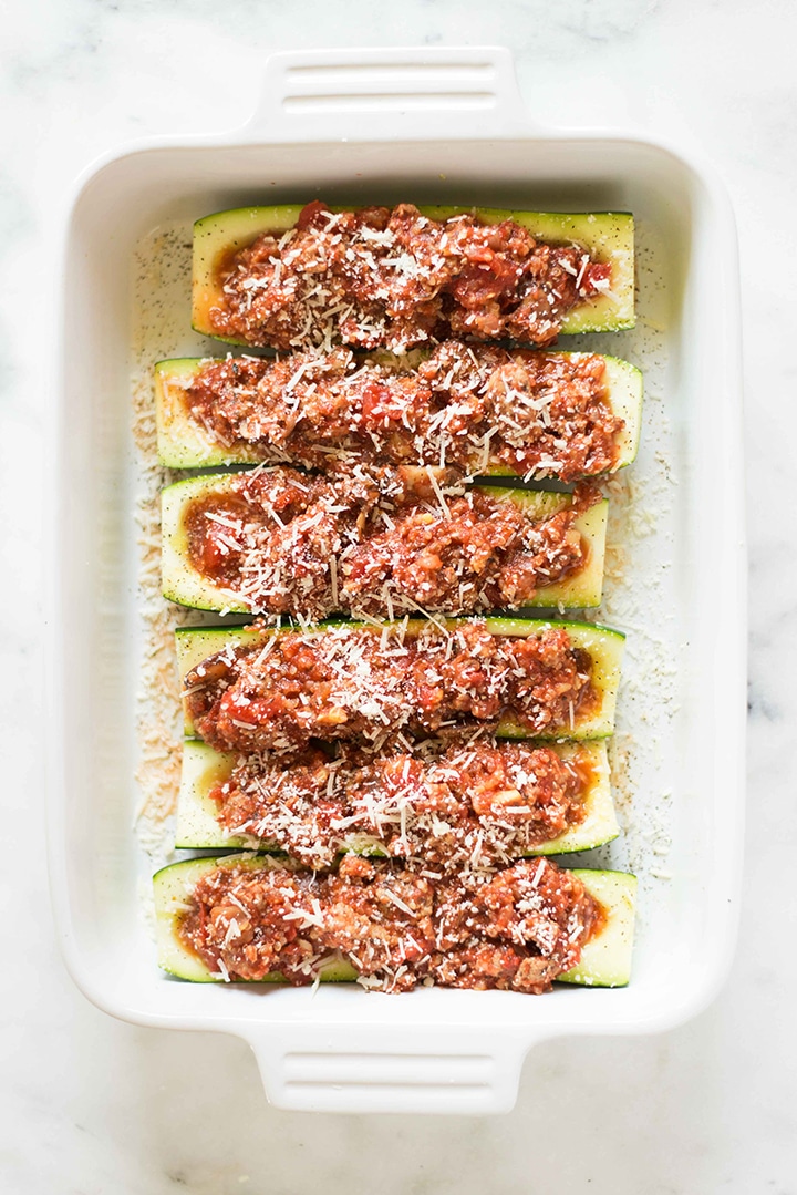Turkey and quinoa stuffed zucchini boats have been topped with freshly grated parmesan cheese and are ready to be placed into the oven to bake.