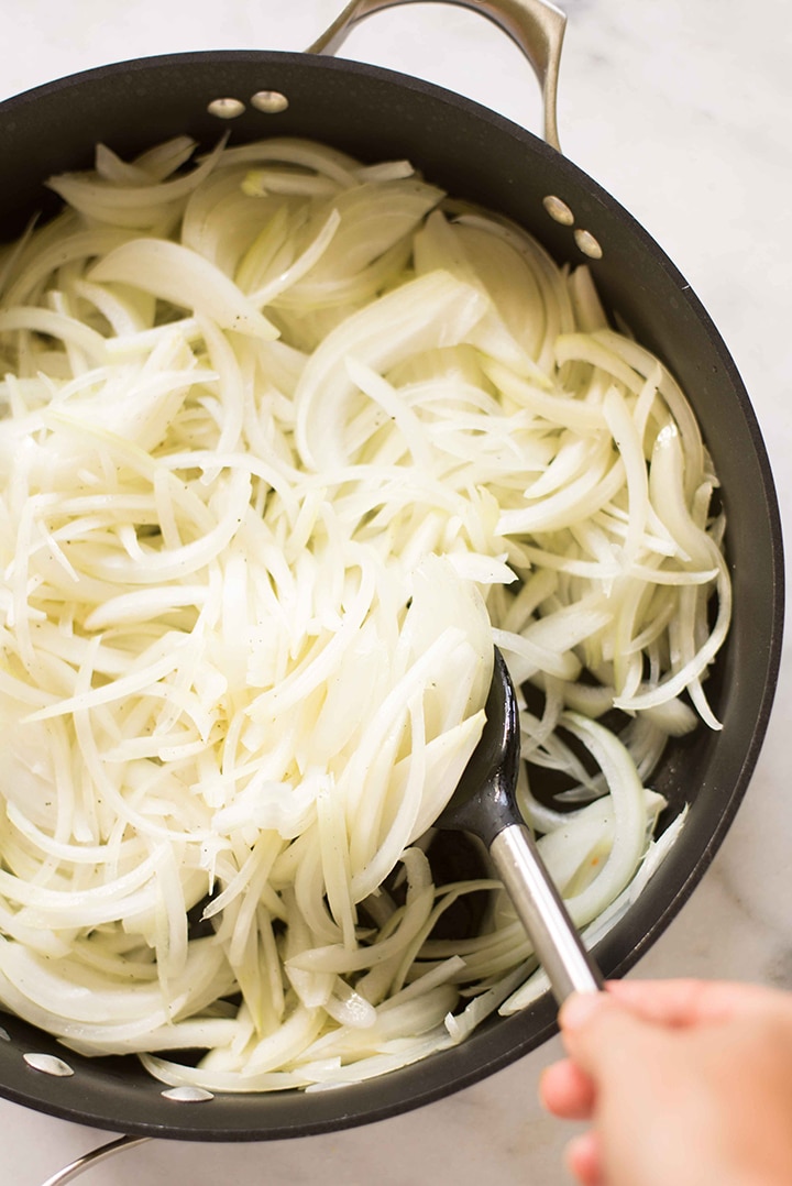 Large skillet filled with thinly sliced yellow onions, ready to be cooked down and caramelized.