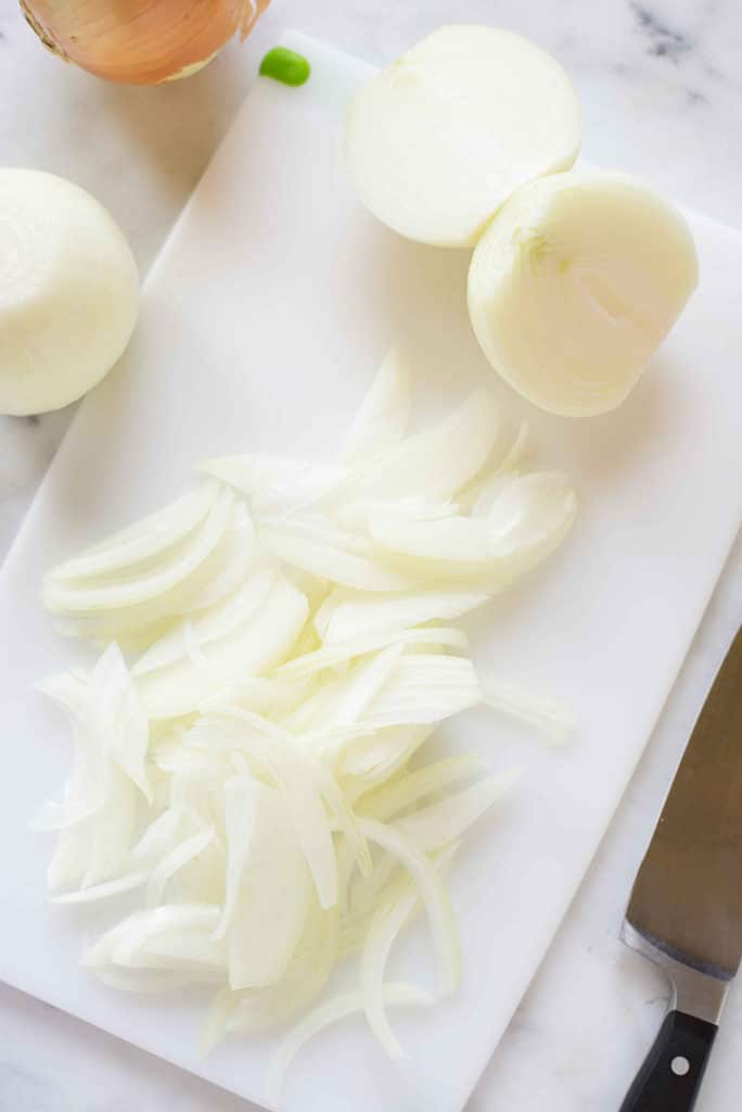 Cutting board with fresh yellow onions that have been thinly sliced to show how thin to slice the onions for certain recipes.