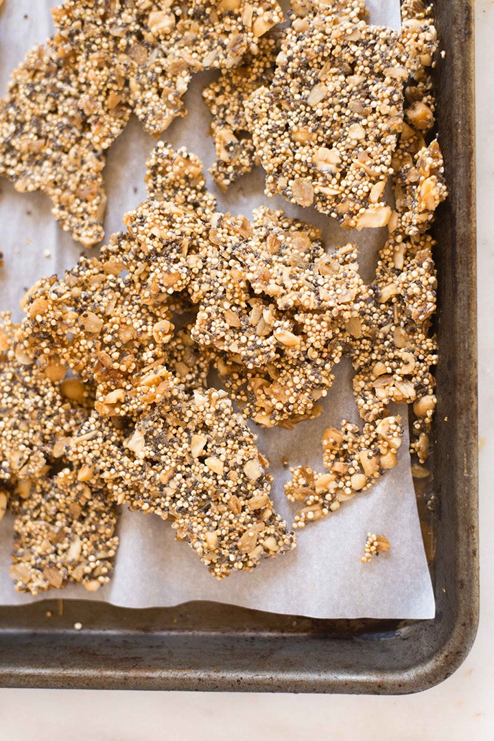Overhead image of a parchment paper lined baking sheet, with Quinoa Peanut Brittle broken up into pieces.
