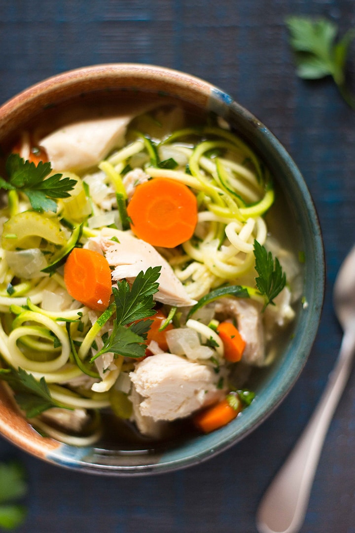 Close up overhead view of a large bowl filled with slow cooker chicken noodle soup, with carrots and zucchini noodles.