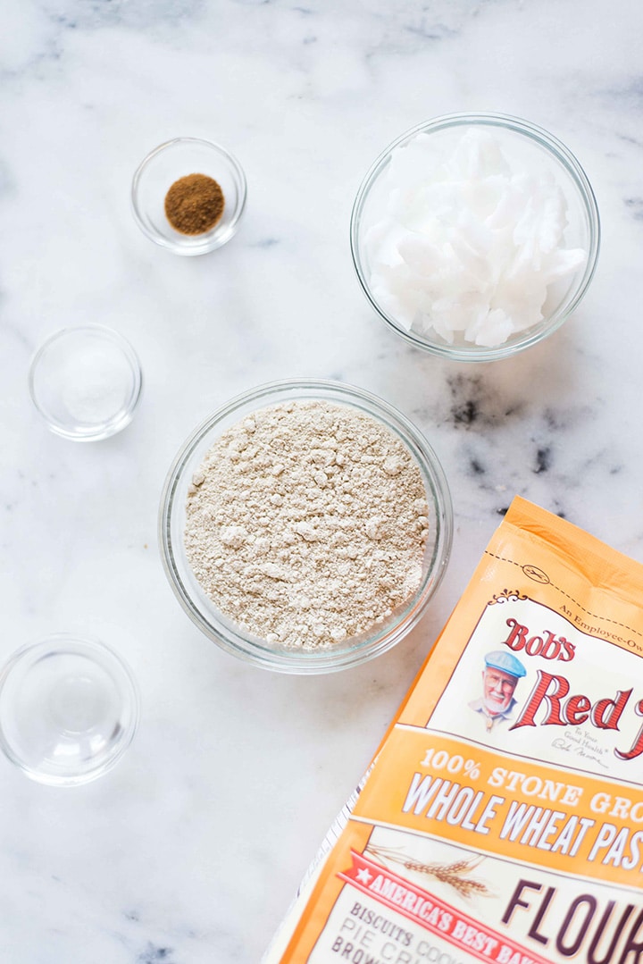 Overhead shot of the ingredients required to make the whole wheat pastry flour crust, including whole wheat pastry flour, hardened coconut oil, sea salt, coconut sugar, and ice water.