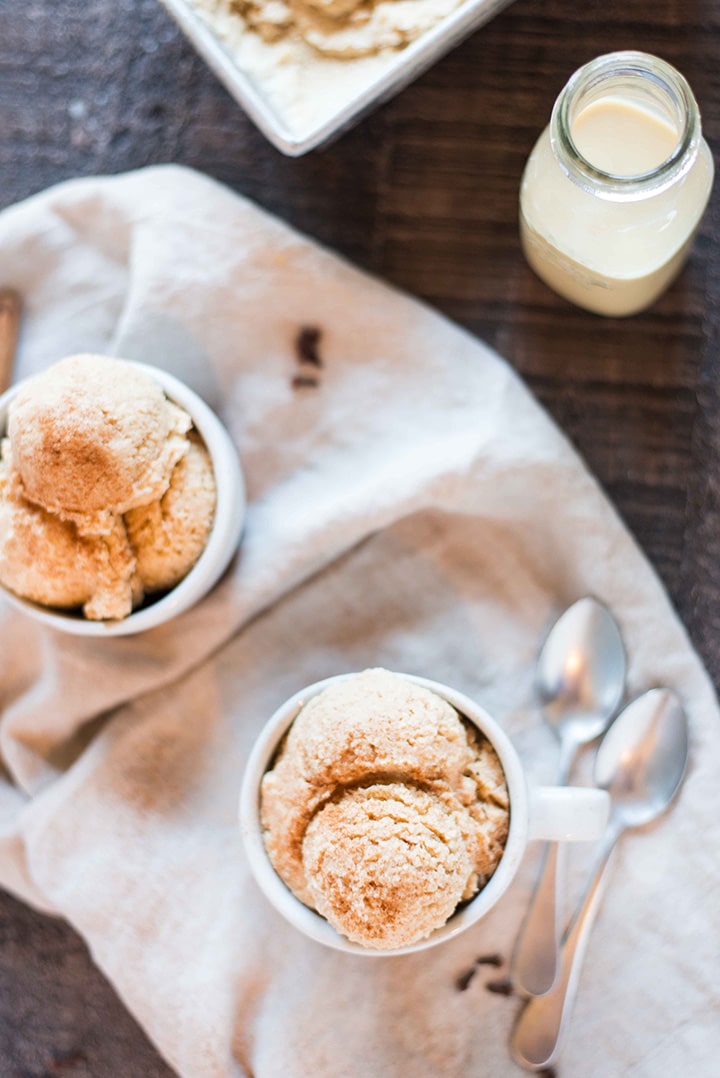 Two scoops of eggnog ice cream, ready to serve, and next to a container of homemade eggnog.
