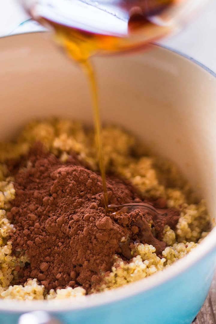 Pouring the pure maple syrup and unsweetened cocoa powder into the saucepan that has the cooked quinoa.
