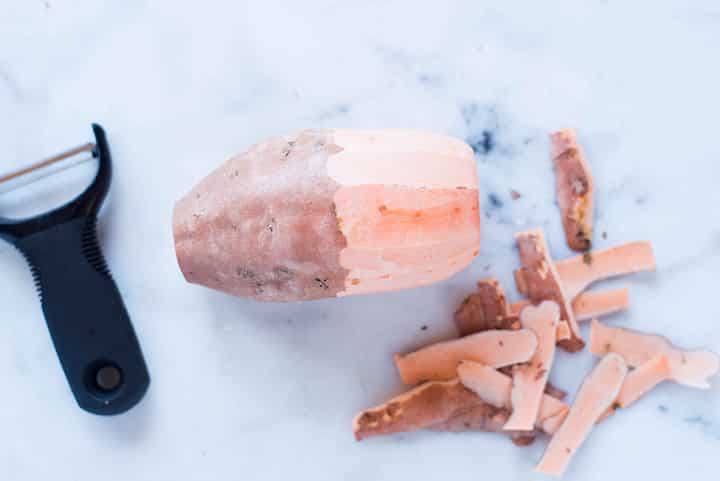 One sweet potato with half the skin peeled off to show the difference for peeling versus not peeling the sweet potato.