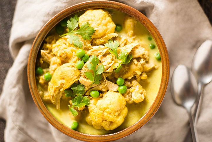 Close up of slow cooker chicken cauliflower curry with peas and topped with fresh cilantro.