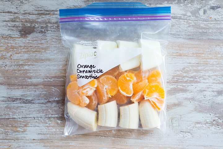 An overhead image of a smoothie freezer pack lying on the kitchen counter with the ingredients for the Orange Dreamsicle Smoothie including peeled mandarin oranges, banana and plain greek yogurt.
