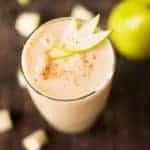 Spiced pear fruit smoothie which is next to diced and whole pears and is topped with ground cinnamon and fresh pear slices.