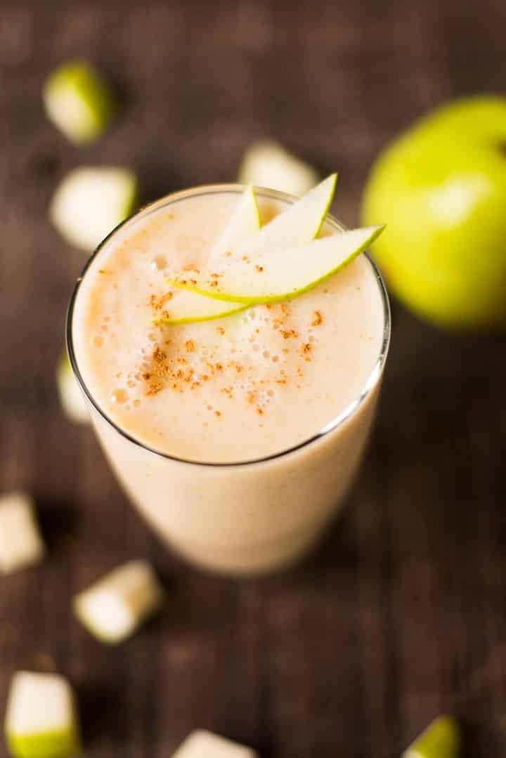 Spiced pear fruit smoothie which is next to diced and whole pears and is topped with ground cinnamon and fresh pear slices.