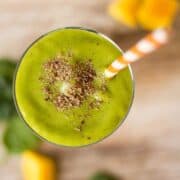 Mango Green Smoothie that is topped with extra flaxseed meal and is next to frozen mango chunks and fresh baby spinach.