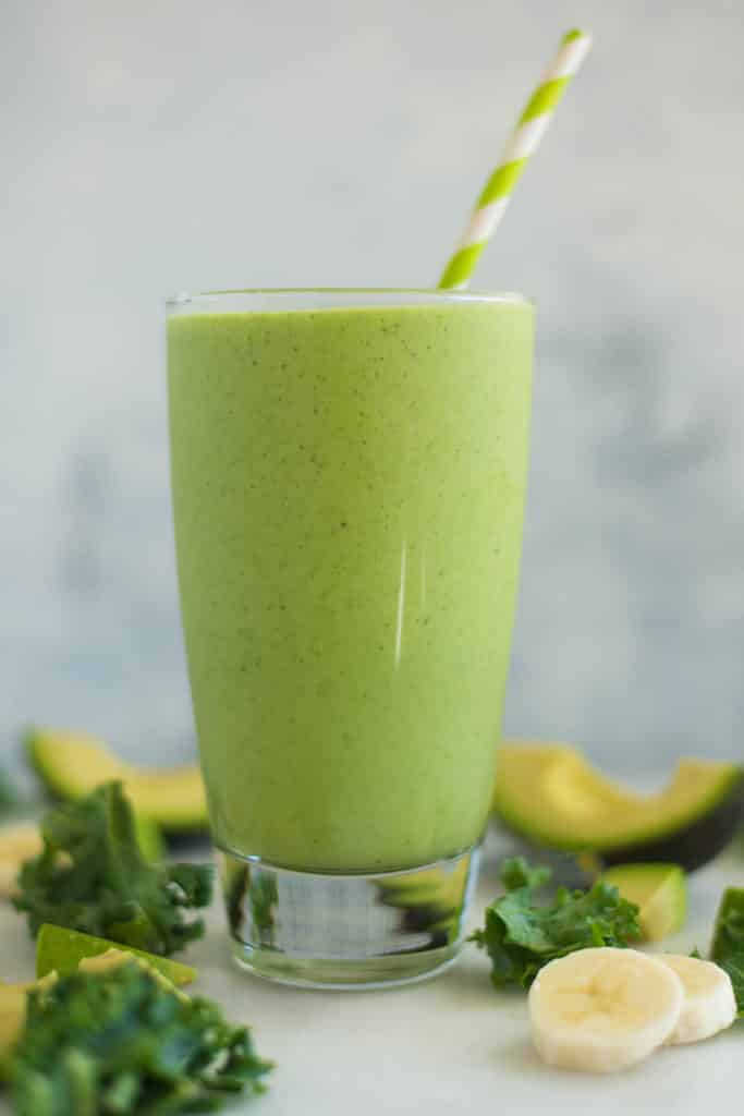 A side image of a glass filled with Avocado Kale Smoothie with kale, banana, avocado, almond milk and lemon juice.