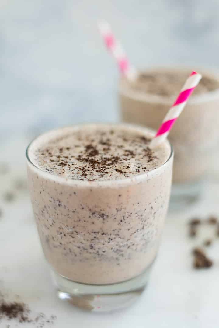 A side image of a glass of Coffee Bean Smoothie with banana, coffee grounds, almond butter, vanilla extract and almond milk topped with a sprinkle of ground coffee.