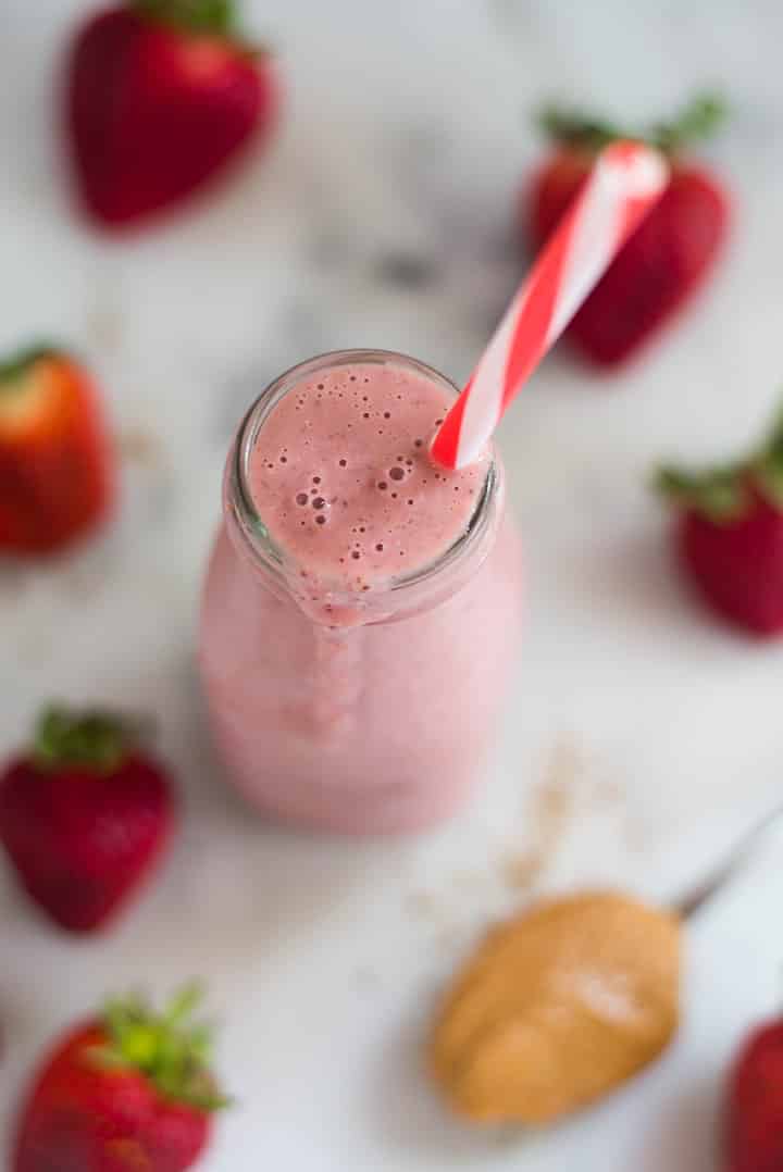 A glass bottle overflowing with the PB&J Smoothie with strawberries, flaxseed meal, peanut butter, oats and almond milk.