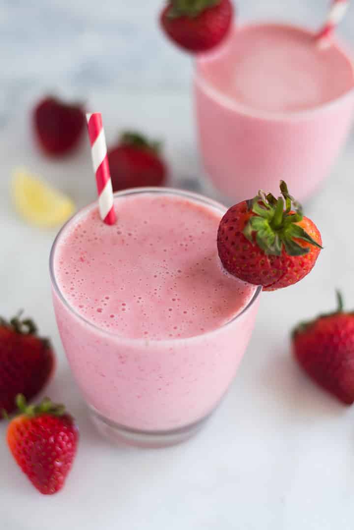 A glass of Strawberry Cheesecake Smoothie with strawberries, greek yogurt, raw honey and lemon juice decorated with a fresh strawberry.