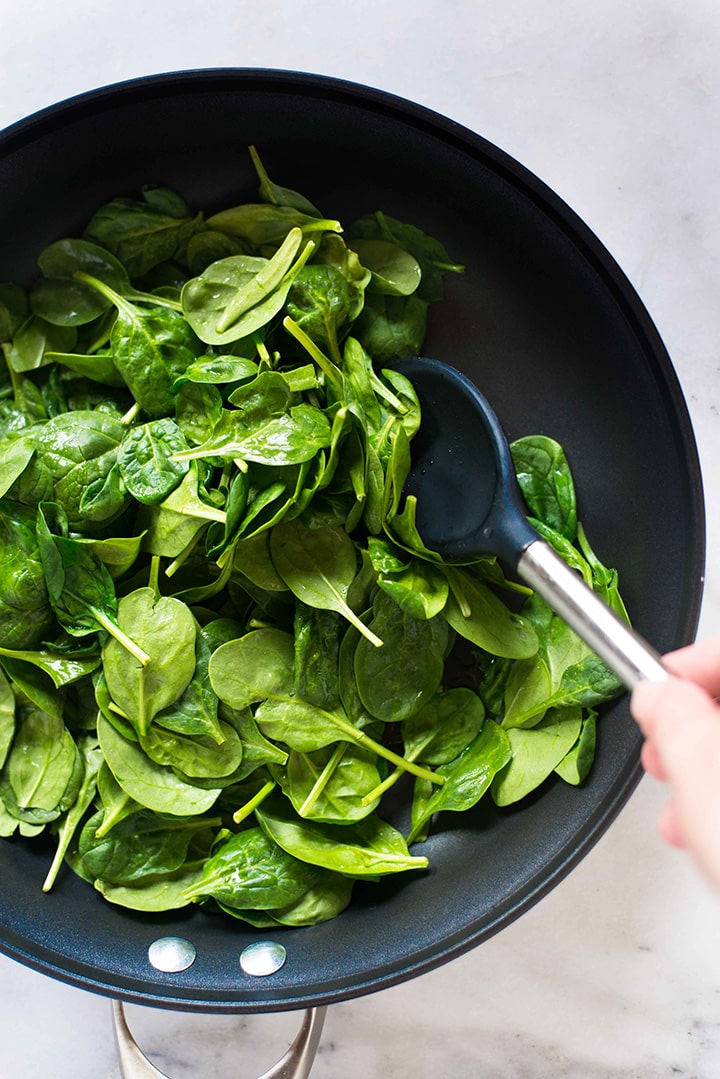 Baby spinach getting tossed with water in a skillet over medium-high heat to wilt and then blend to use in the homemade spinach tortillas.
