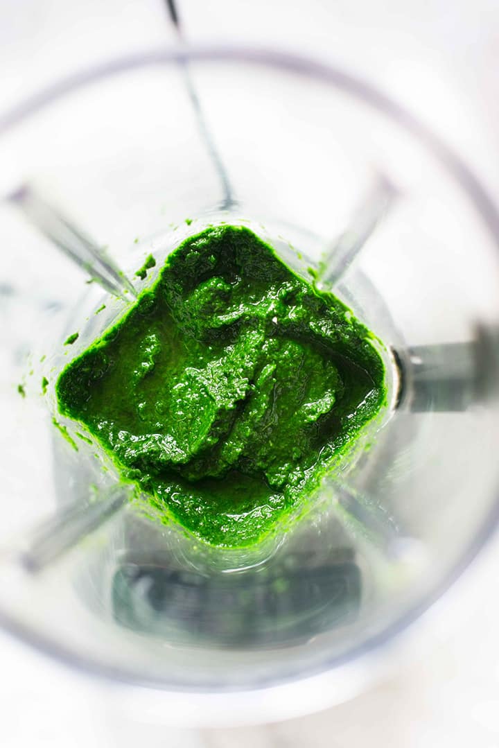 Overhead view of a kitchen blender with pureed cooked baby spinach and water. This mixture will be added to the spelt flour to make the homemade spinach tortillas.