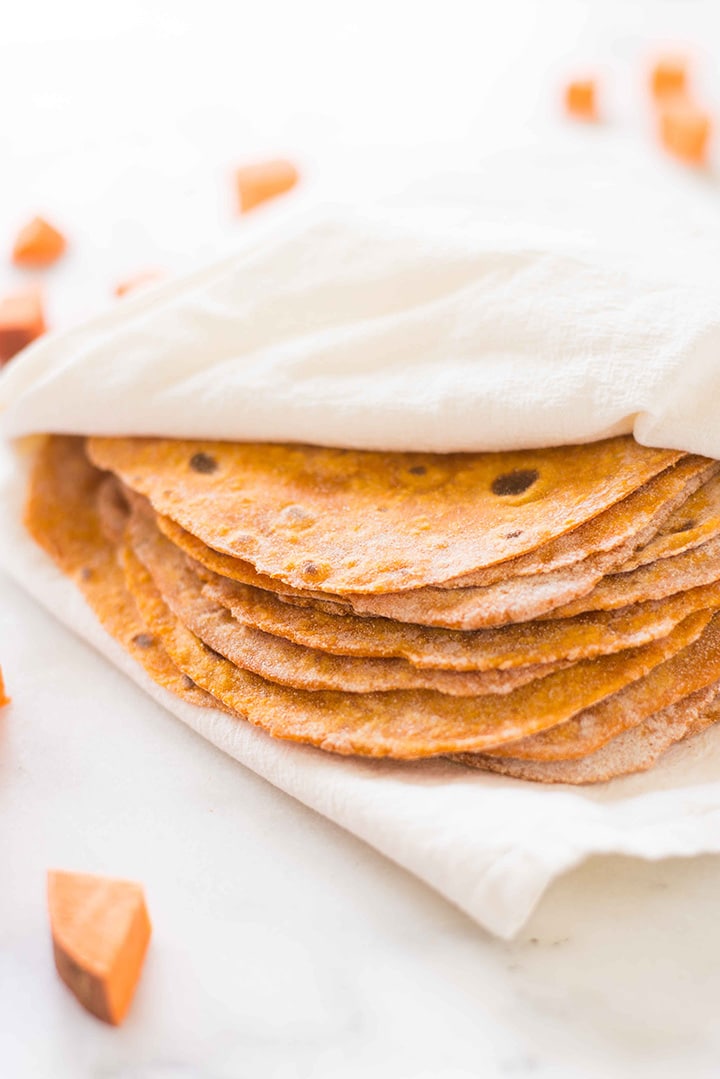 Kitchen towel wrapping the sweet potato tortillas alongside diced raw sweet potato.