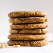 Peanut butter paleo cookies stacked on top of each other, setting next to raw peanuts.