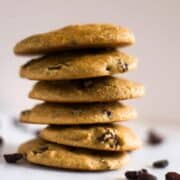 No oatmeal oatmeal raisin paleo cookies stacked on top of each other, setting next to raisins.